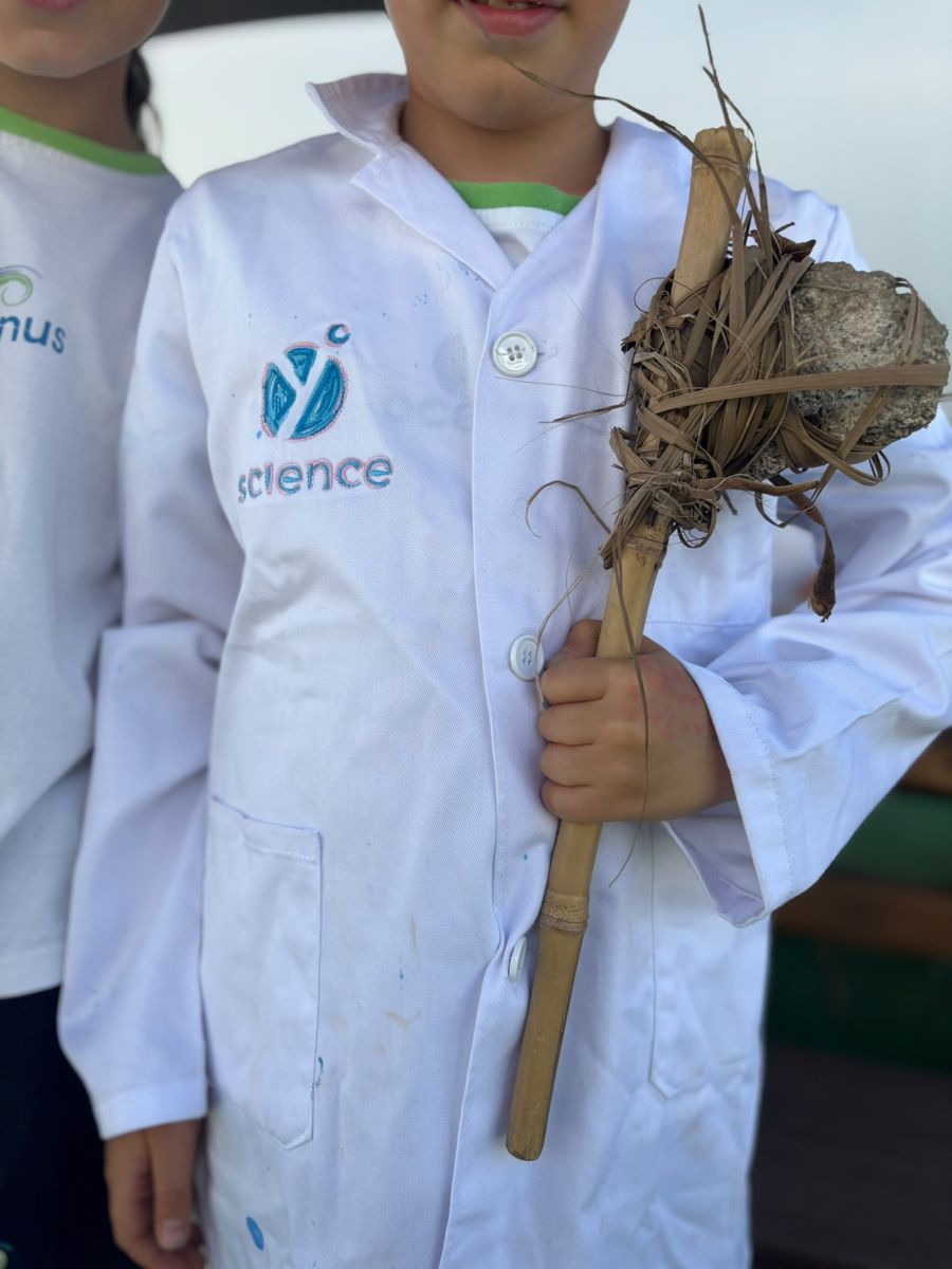 Aluno de bata YScience com um machado construído em cana e pedra